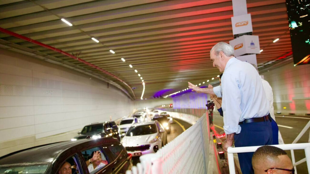 Hombre saluda a coches en túnel iluminado.