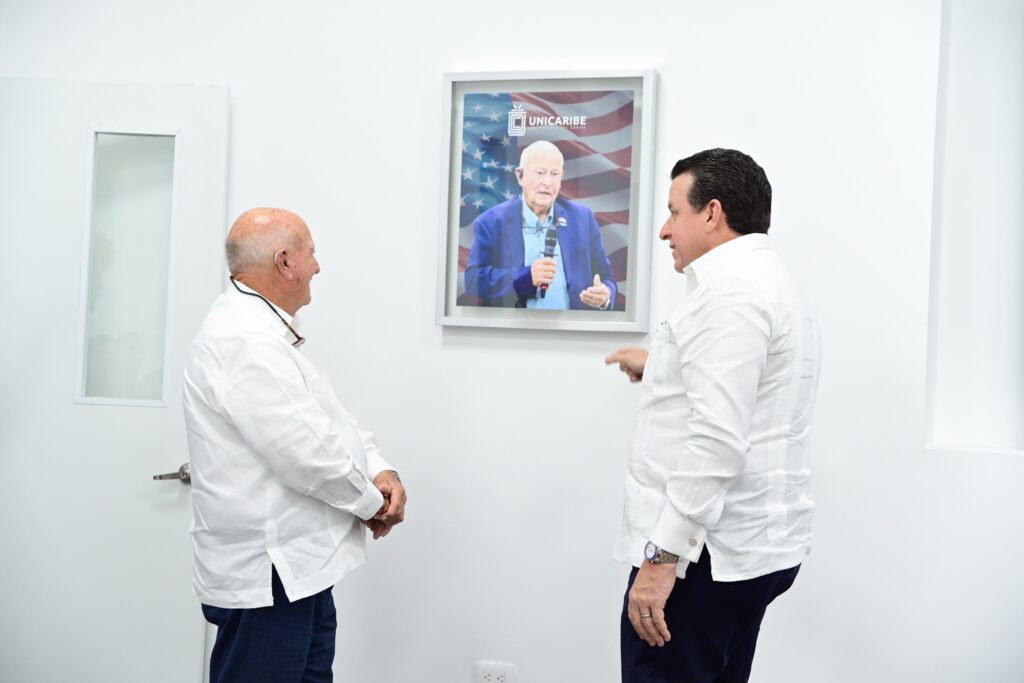 Dos hombres observando un retrato de un anciano con la bandera estadounidense.