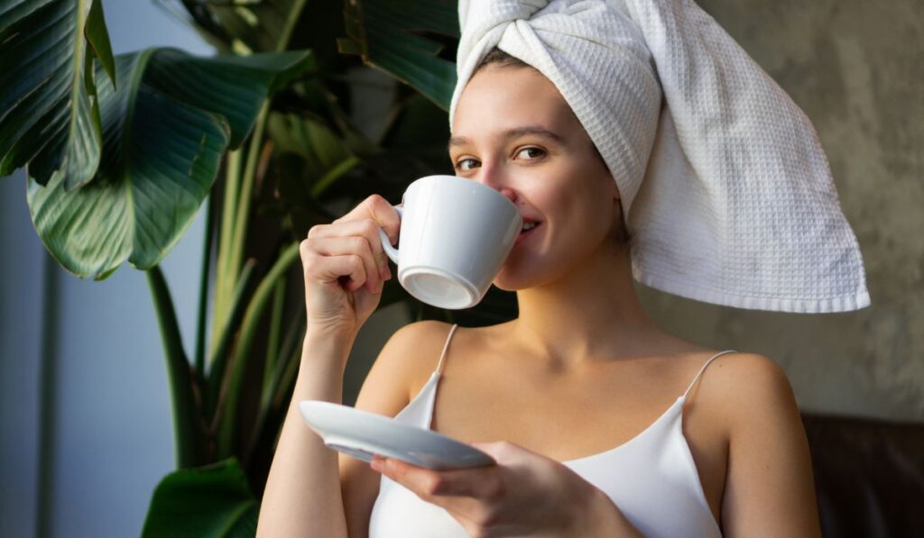 Mujer sonriendo bebe café con toalla en la cabeza