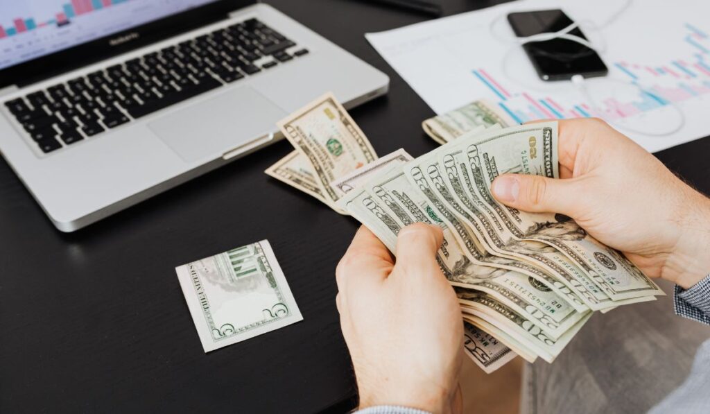 Man counting dollars near laptop and charts.