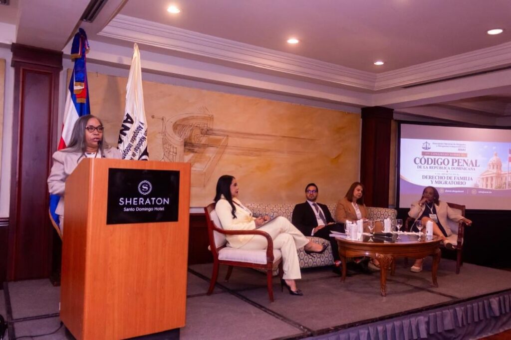 Mujer dando discurso en estrado con panel de expertos detrás.