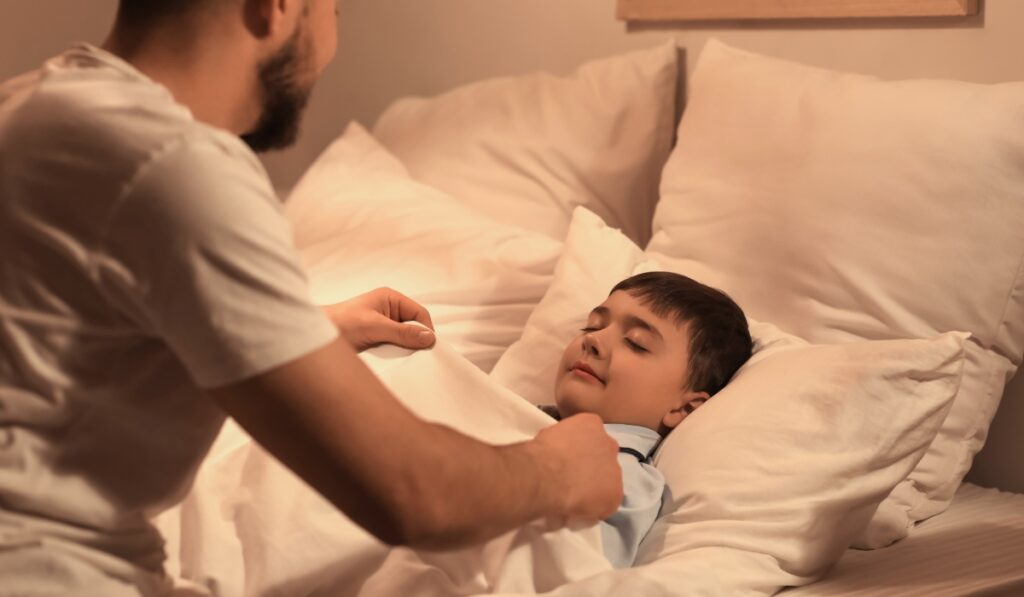 Padre arropando a su hijo en la cama.