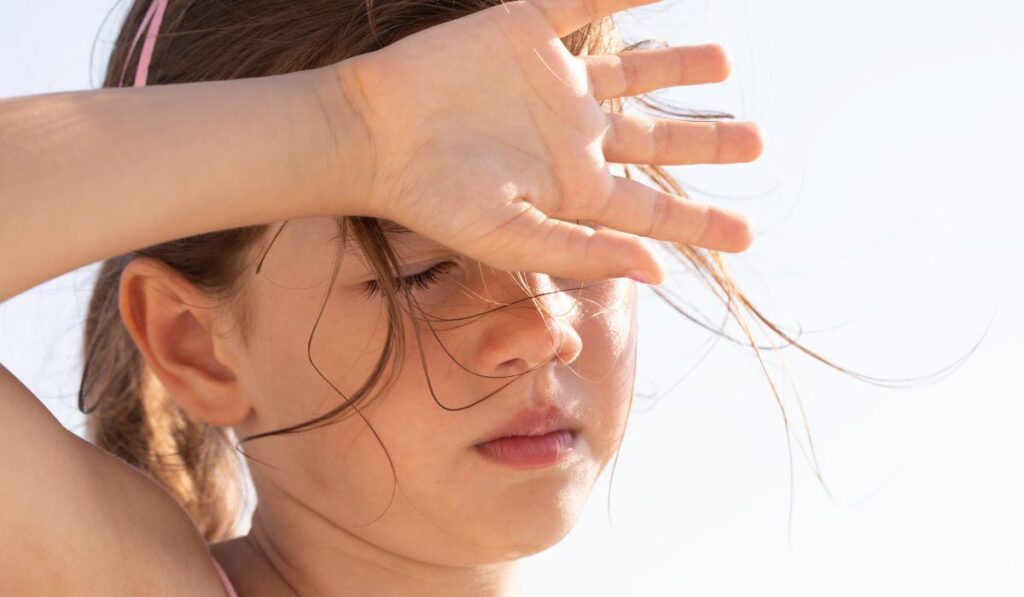 Niña se cubre los ojos del sol con la mano.