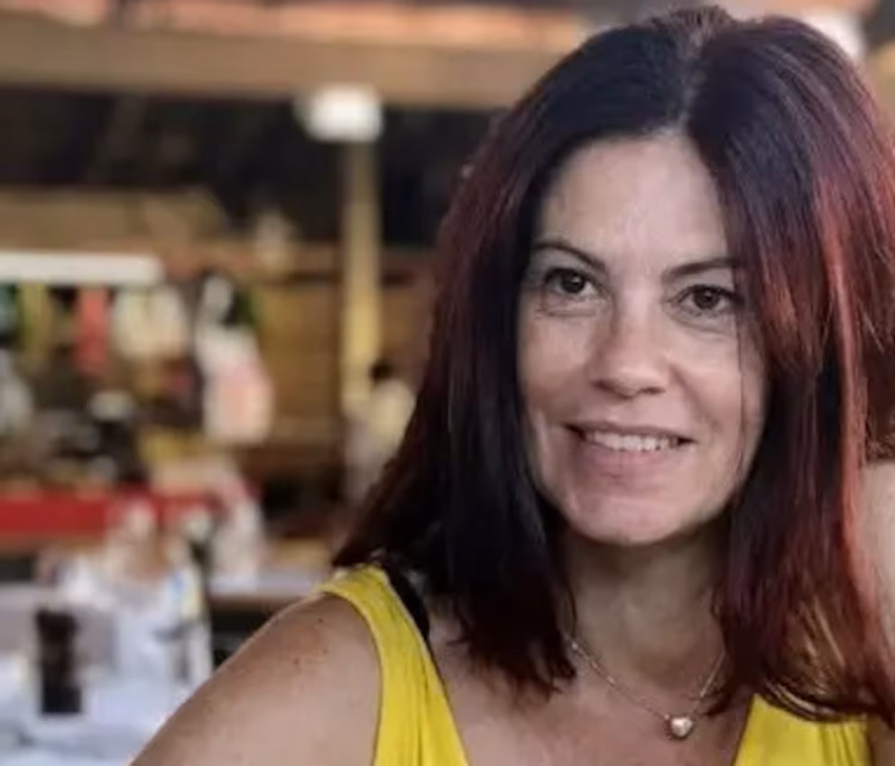 Mujer sonriendo con cabello oscuro y blusa amarilla.
