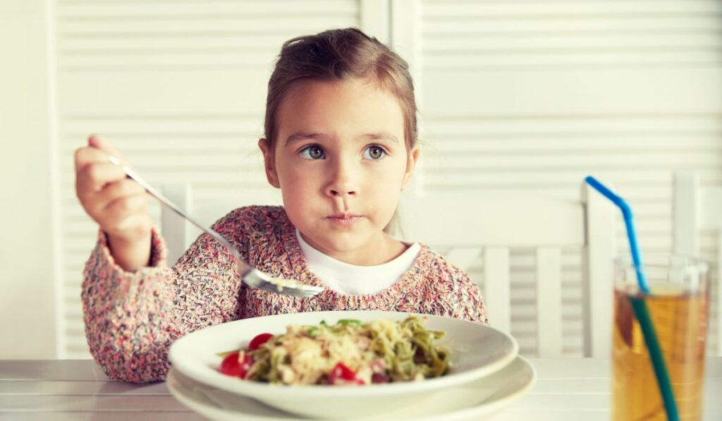Niña comiendo pasta con tenedor en un plato.
