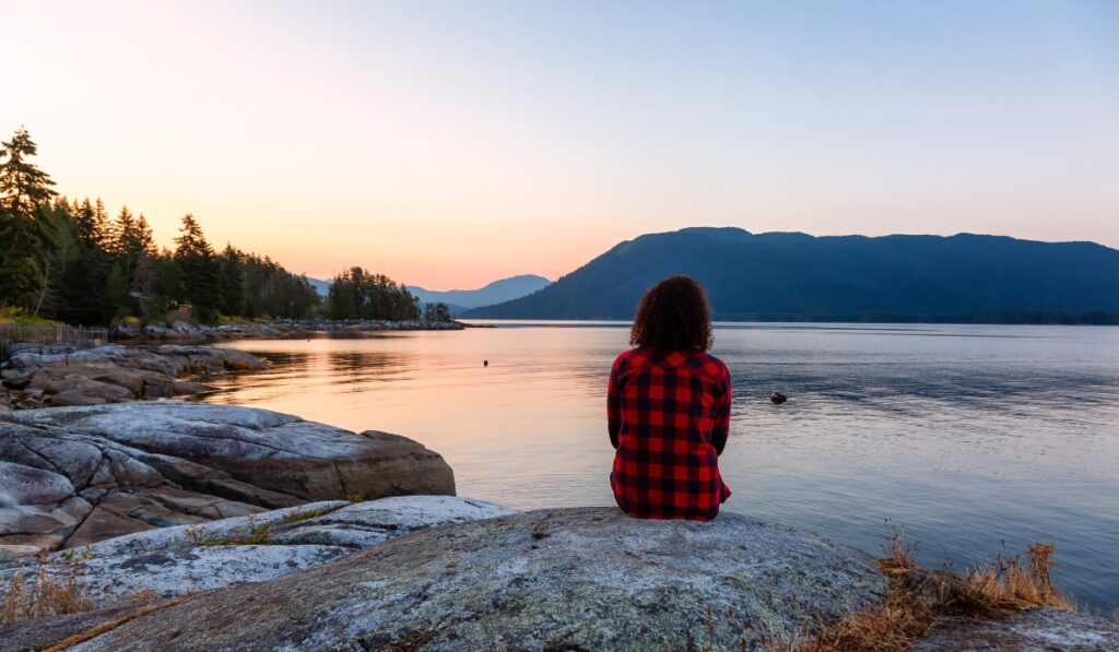 Mujer con camisa de cuadros rojos y negros mira el amanecer sobre el agua.