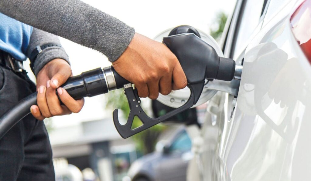 Persona repostando combustible a un coche en una gasolinera.