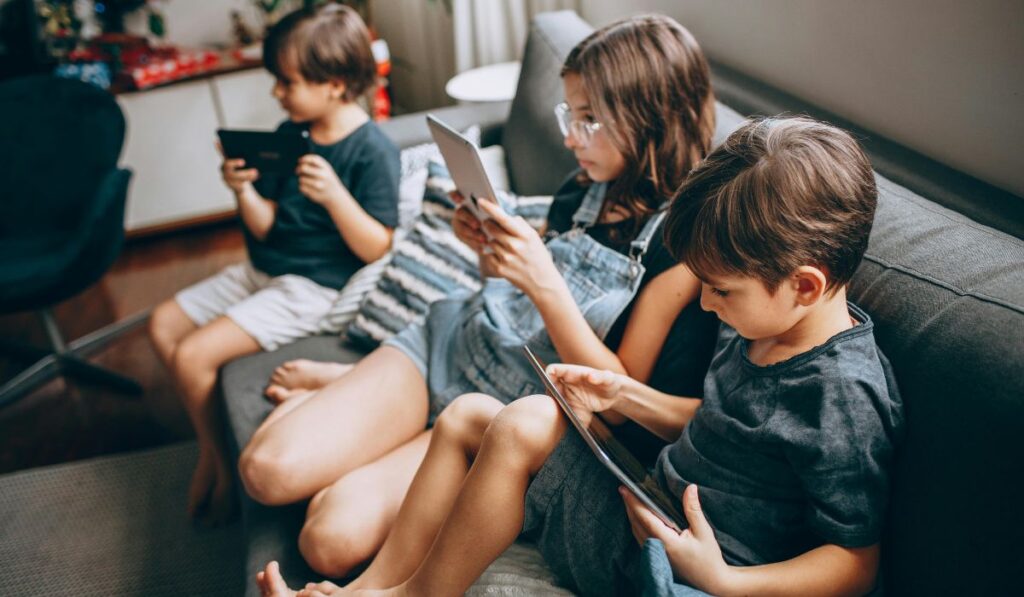 Tres niños sentados en un sofá usando tabletas.