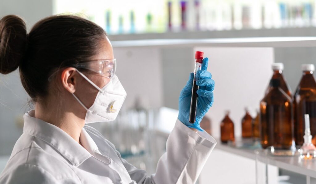 Científica con mascarilla y gafas examinando un tubo de ensayo.