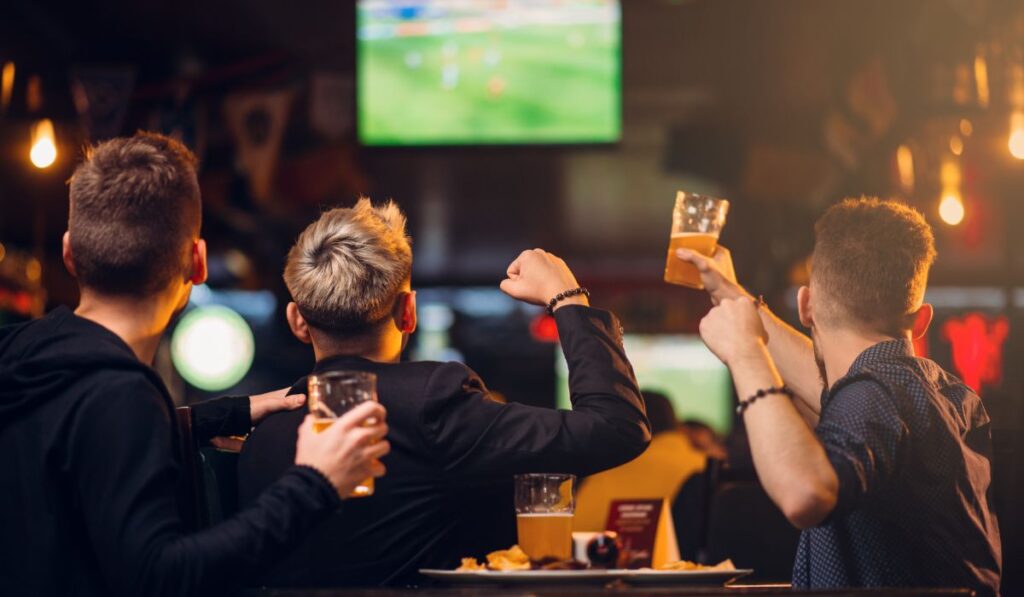 Amigos viendo un partido de fútbol en un bar con cerveza.