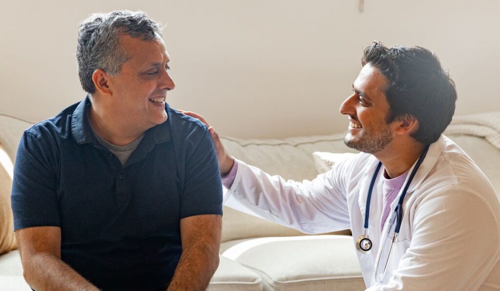Médico de bata blanca habla con paciente sonriente en un sofá.