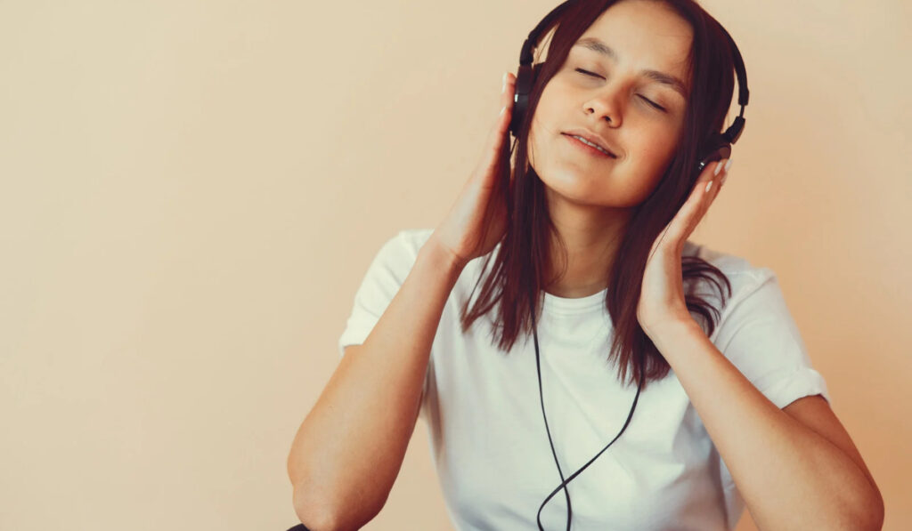 Mujer joven con auriculares escuchando música con los ojos cerrados.