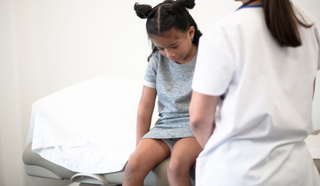 Niña sentada en camilla médica mirando hacia abajo