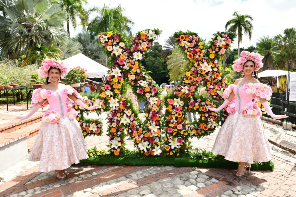 Dos mujeres vestidas de rosa junto a letras florales enormes.