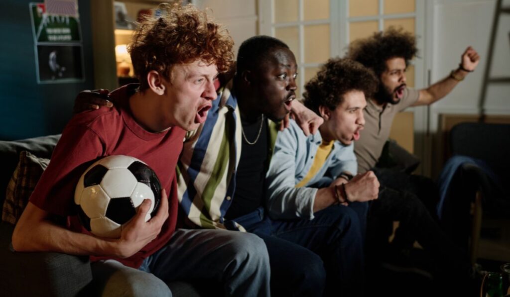 Amigos mirando un partido de fútbol, emocionados y gritando
