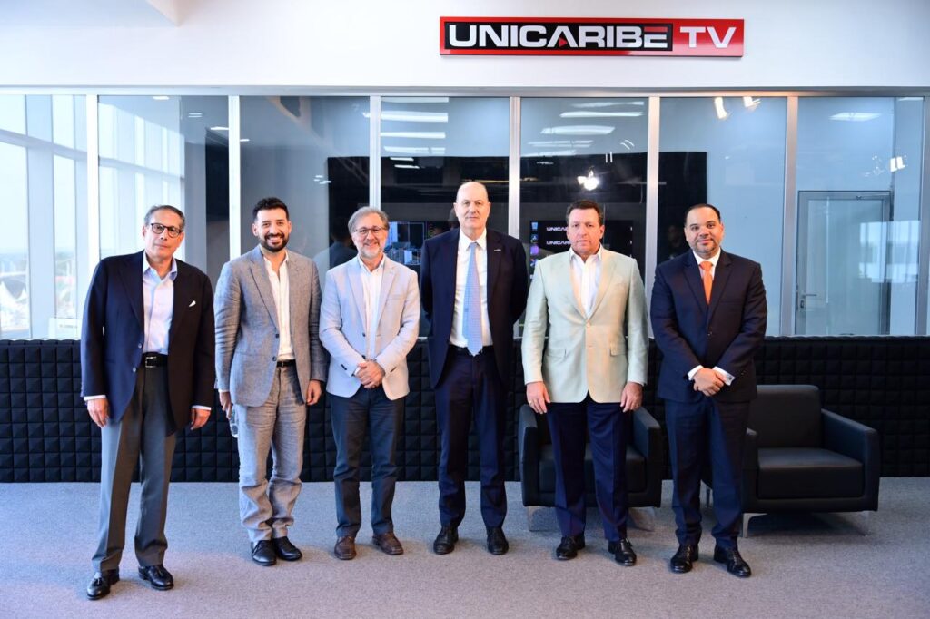 Un equipo de hombres de negocios posa frente al logo de Unicaribe TV.