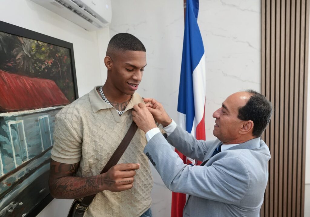 Hombre colocando un pin a otro hombre frente a una bandera.