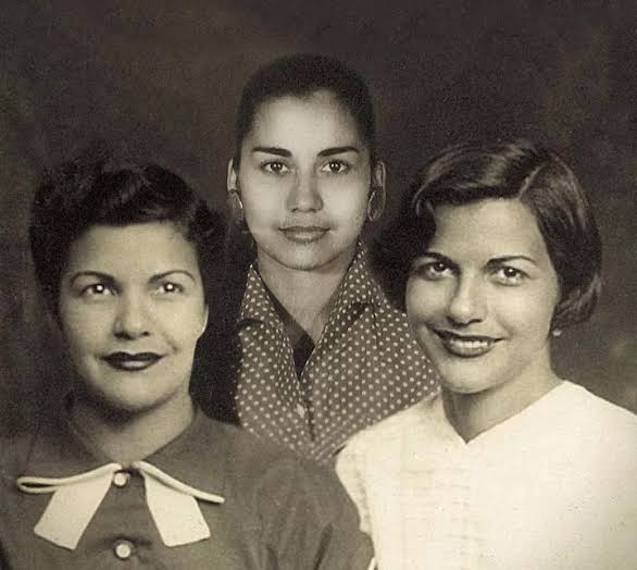 Tres mujeres jóvenes sonriendo en un retrato de estudio antiguo.