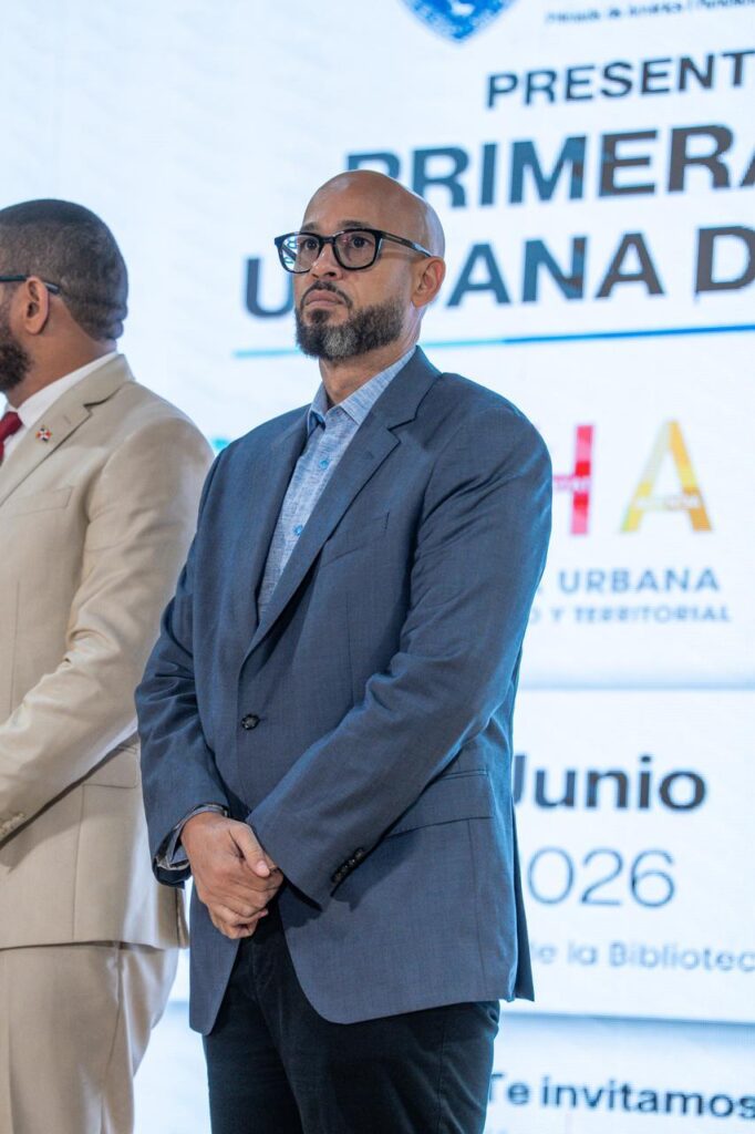 Hombre con gafas y barba, traje azul, atento en un evento.