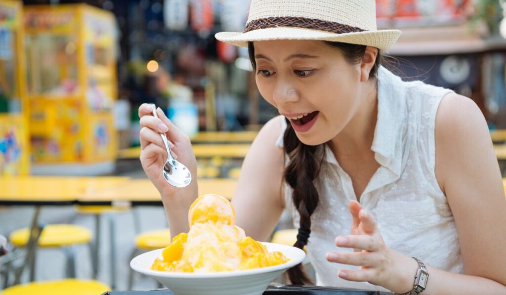 Mujer asiática con sombrero disfrutando un postre helado.