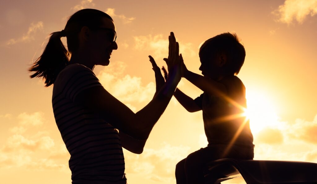 Silueta de madre e hijo dándose las cinco al atardecer.