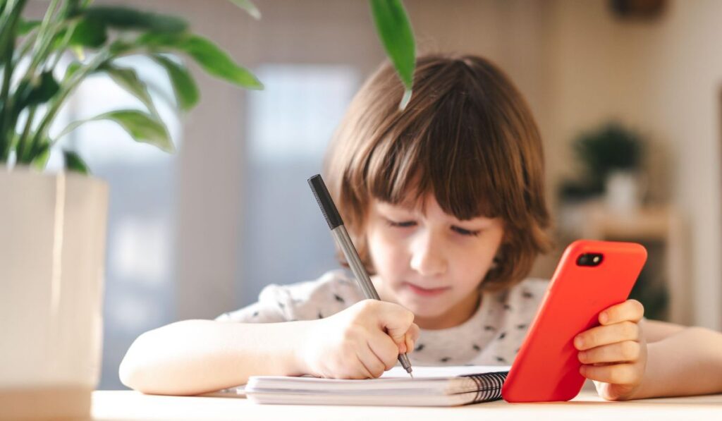 Niño con móvil rojo escribe en cuaderno