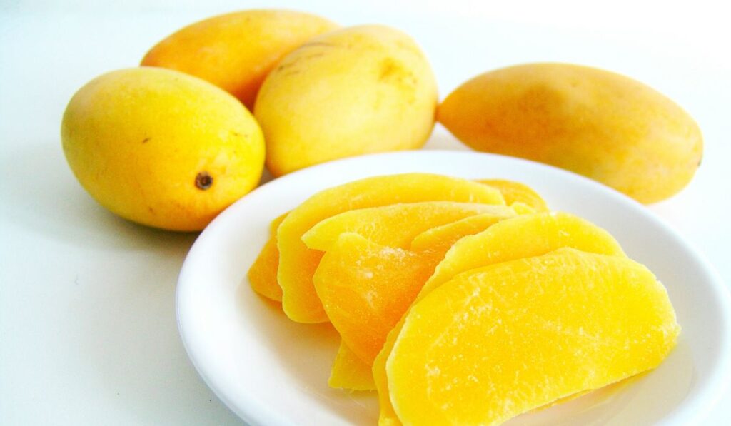 Mangos enteros y cortados en rodajas en un plato blanco.