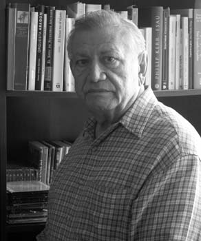 Retrato de un hombre mayor frente a una estantería de libros.