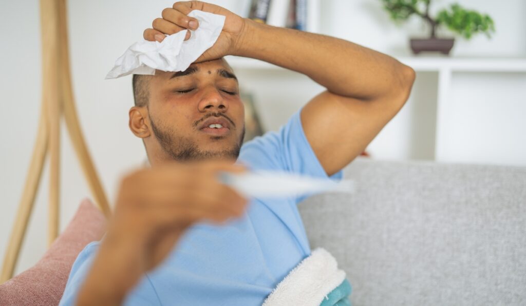 Hombre con fiebre se aplica compresa fría en la frente.