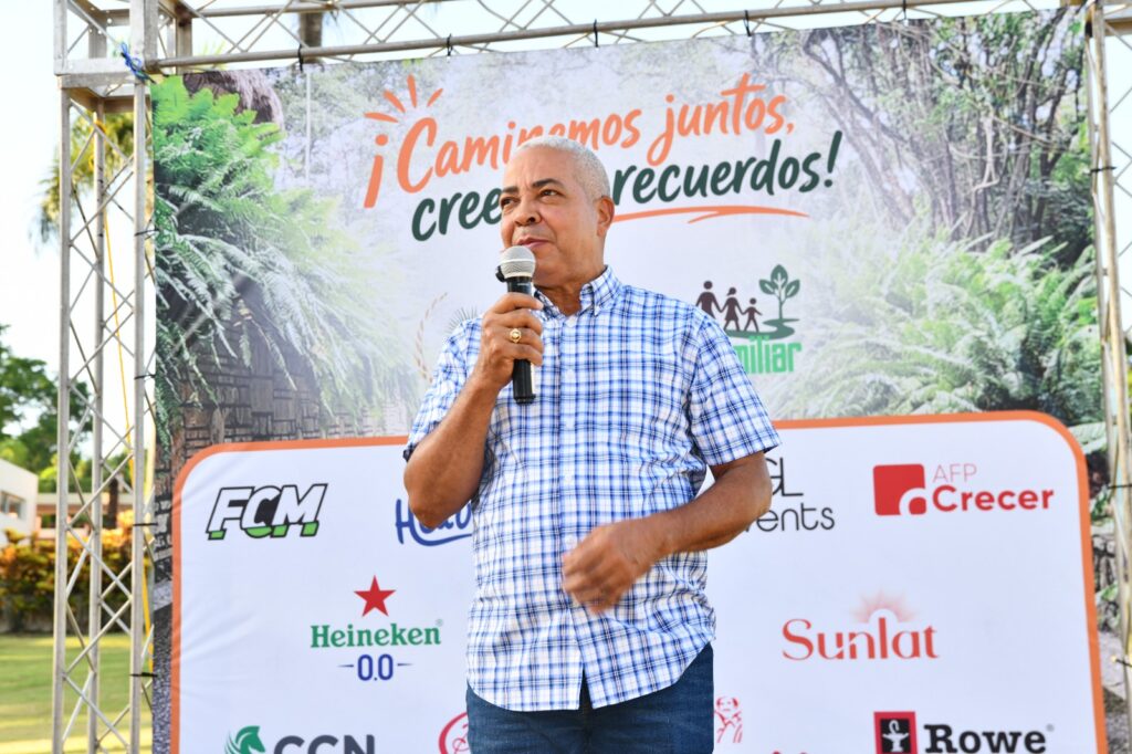 Hombre hablando por micrófono frente a un telón de fondo de naturaleza.
