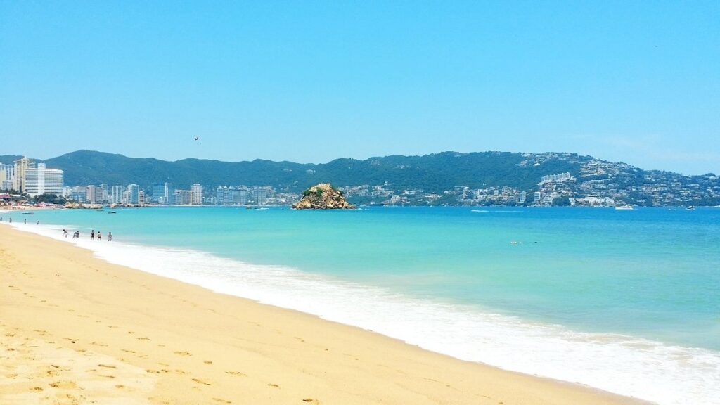 Playa soleada con aguas turquesas y edificios en la costa.