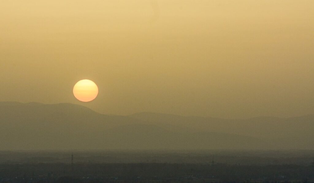 Sol poniente sobre montañas en un cielo crepuscular.