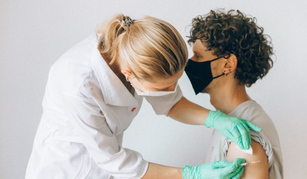 Una enfermera administra una vacuna a un paciente con mascarilla.