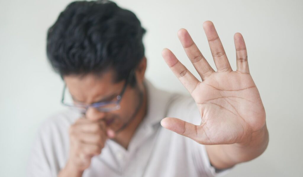 Hombre tosiendo y levantando la mano en señal de parada.