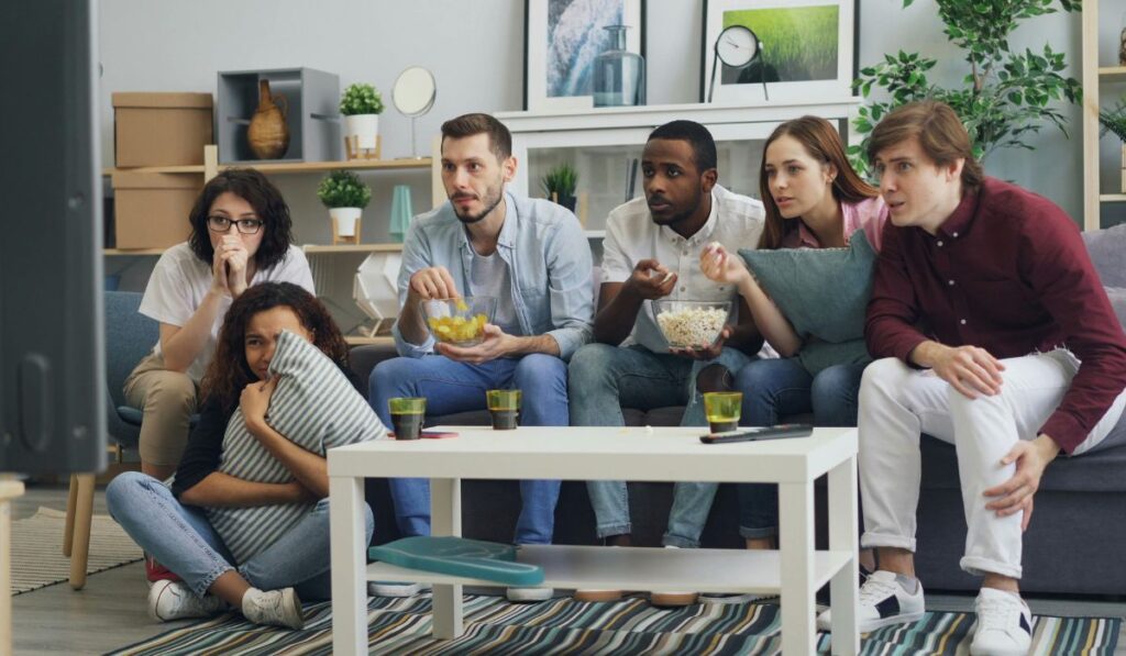 Grupo de amigos mirando televisión con expresión de miedo.
