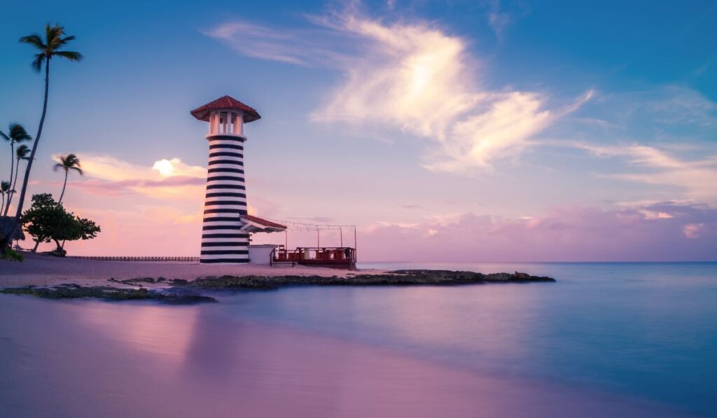 Faro a rayas blancas y negras en la playa al atardecer.