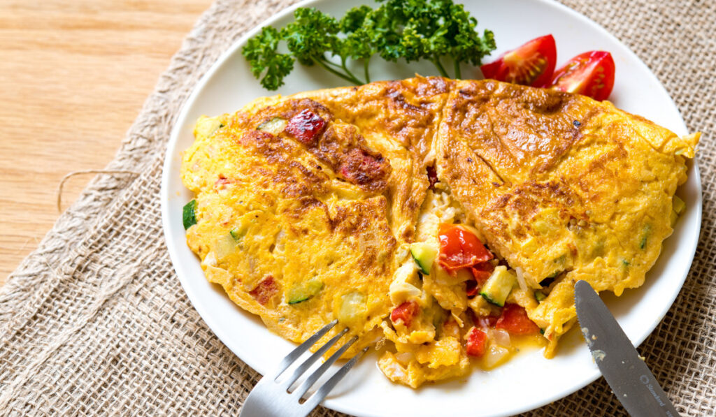 Tortilla francesa dorada con verduras y tomate fresco.