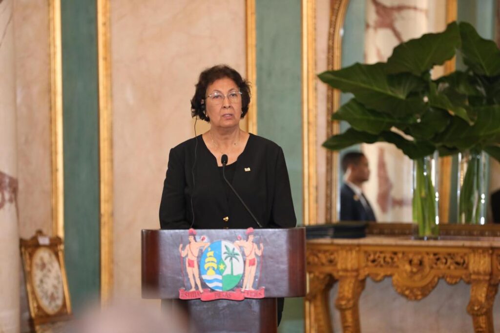 Mujer con gafas habla en un podio con escudo.