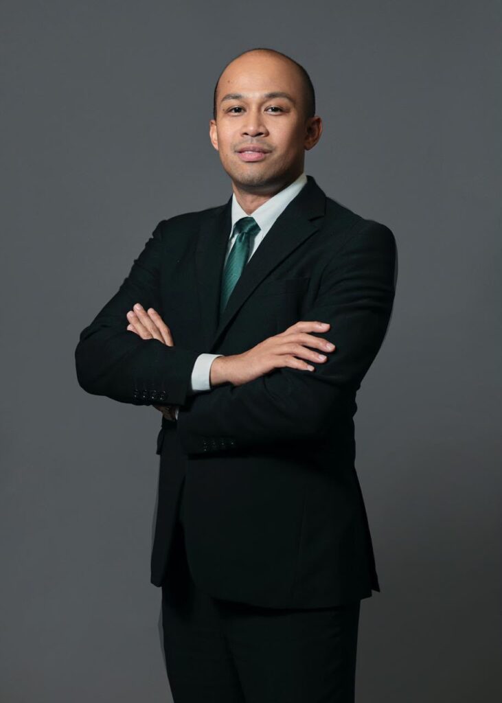 Hombre de negocios con traje negro y corbata verde cruzado de brazos.