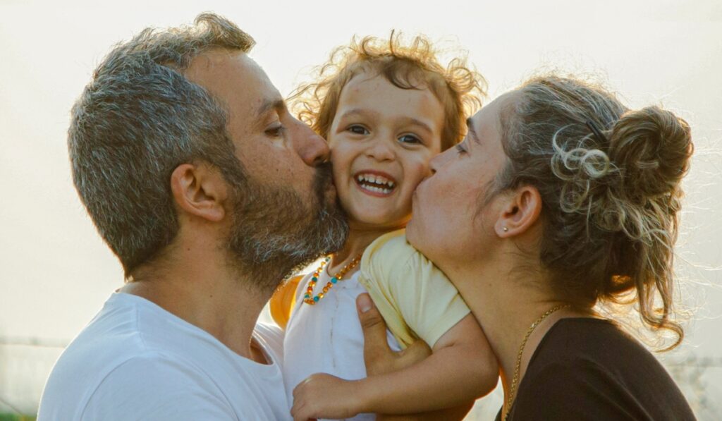 Familia besando a su hija en un día soleado.