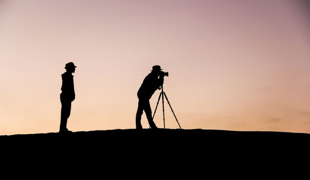 Siluetas de dos hombres, uno fotografiando, al atardecer.