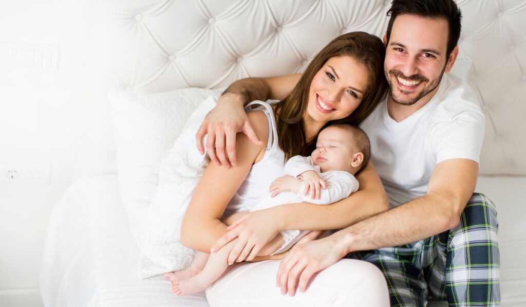 Familia feliz con bebé durmiendo en cama blanca.